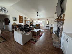 Living room featuring a fireplace, vaulted ceiling, dark wood-style floors, and ceiling fan
