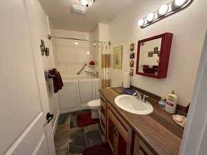 Bathroom with a textured ceiling, vanity, dark stone finish flooring, and shower / tub combo with curtain
