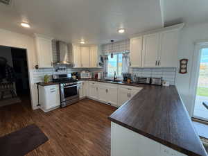 Kitchen featuring white cabinets, decorative backsplash, stainless steel gas stove, a textured ceiling, and wall chimney exhaust hood