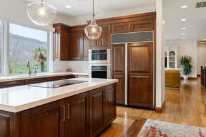 Kitchen featuring paneled fridge, hanging light fixtures, double oven, recessed lighting, and light wood-type flooring