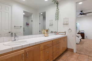 Full bathroom featuring double vanity, light tile patterned floors, a stall shower, ensuite bath, and ceiling fan