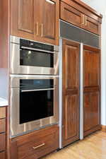 Kitchen with brown cabinetry, paneled fridge, stainless steel double oven, and light wood-type flooring