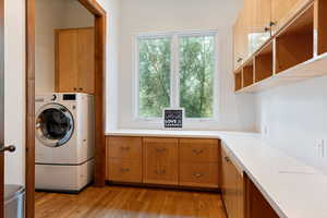 Laundry area featuring light wood-style flooring, washer / dryer, and cabinet space