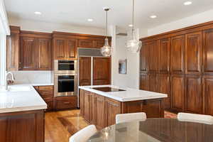Kitchen featuring a center island, decorative light fixtures, light wood-type flooring, double oven, and light stone countertops