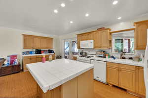 Kitchen with ornamental molding, plenty of natural light, light wood-style floors, recessed lighting, and white appliances