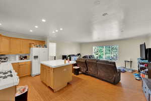 Kitchen with ornamental molding, tile countertops, white fridge with ice dispenser, light wood-style floors, and recessed lighting