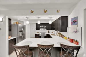 Kitchen featuring a breakfast bar area, appliances with stainless steel finishes, a peninsula, hanging light fixtures, and light stone countertops