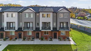 View of front of house featuring a front yard, a balcony, a residential view, and brick siding