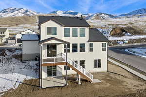Snow covered rear of property with a mountain view, stairway, and a shingled roof
