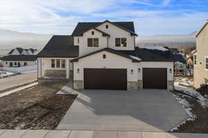 Modern farmhouse style home with stone siding, a mountain view, concrete driveway, and roof with shingles