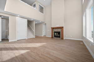 Unfurnished living room with light wood-style flooring, a high ceiling, a fireplace, and stairs