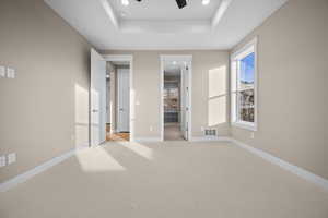 Unfurnished bedroom with ensuite bathroom, a raised ceiling, recessed lighting, ceiling fan, and light carpet