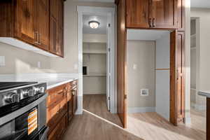 Kitchen featuring stainless steel gas stove, brown cabinets, light wood-type flooring, and light stone counters