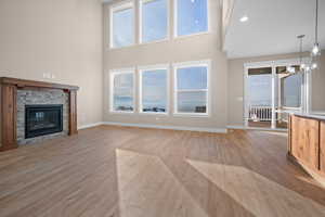 Unfurnished living room featuring light wood-type flooring, a glass covered fireplace, a high ceiling, a chandelier, and recessed lighting