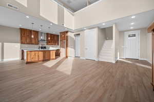 Kitchen with open floor plan, brown cabinetry, a center island with sink, light countertops, and hanging light fixtures