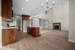 Kitchen with pendant lighting, a center island with sink, a fireplace, light wood finished floors, and a towering ceiling