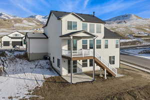 Snow covered house featuring a patio area, stairs, a deck with mountain view, and stucco siding