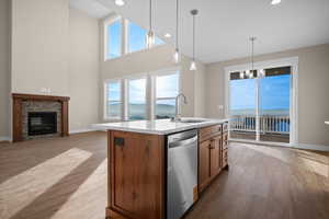 Kitchen featuring decorative light fixtures, dishwasher, light wood-style flooring, brown cabinetry, and a brick fireplace