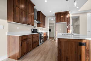 Kitchen with range with two ovens, wall chimney exhaust hood, light stone countertops, light wood-type flooring, and decorative light fixtures