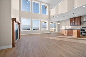 Kitchen featuring a kitchen island with sink, pendant lighting, open floor plan, wall chimney exhaust hood, and light wood-type flooring