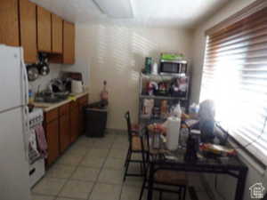 Kitchen with brown cabinets, white appliances, light tile patterned flooring, and light countertops
