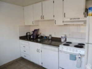 Kitchen featuring white appliances, dark countertops, ventilation hood, tasteful backsplash, and white cabinetry