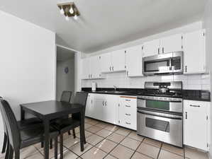 Kitchen featuring stainless steel appliances, backsplash, dark countertops, light tile patterned floors, and white cabinets