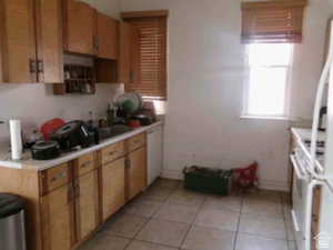 Kitchen with light tile patterned floors, light countertops, white appliances, and brown cabinetry