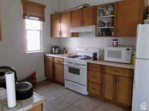 Kitchen with brown cabinets, white appliances, light countertops, light tile patterned flooring, and ventilation hood