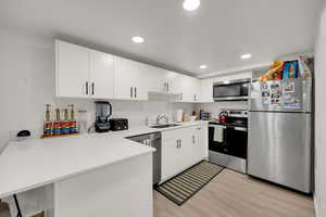 Kitchen with appliances with stainless steel finishes, white cabinets, light wood-type flooring, a peninsula, and recessed lighting