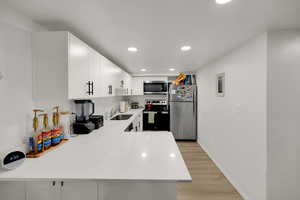 Kitchen featuring stainless steel appliances, light wood-style floors, recessed lighting, white cabinetry, and light stone countertops