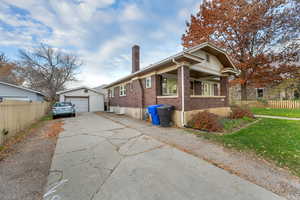 View of front of house with a chimney, brick siding, a detached garage, an outbuilding, and concrete driveway