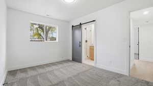 Unfurnished bedroom with a barn door, carpet, and ensuite bathroom