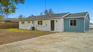 Rear view of house with board and batten siding, a shingled roof, and a patio