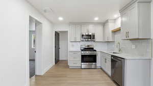 Kitchen with stainless steel appliances, light stone counters, decorative backsplash, light wood-type flooring, and recessed lighting