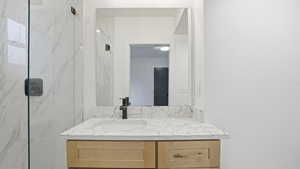 Bathroom featuring vanity and a marble finish shower