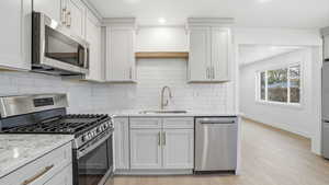 Kitchen with stainless steel appliances, light stone counters, light wood-style flooring, backsplash, and recessed lighting