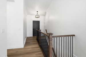 Corridor featuring an upstairs landing, wood finished floors, a chandelier, and lofted ceiling