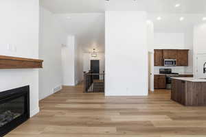 Kitchen featuring stainless steel appliances, a glass covered fireplace, a high ceiling, light wood finished floors, and dark brown cabinets