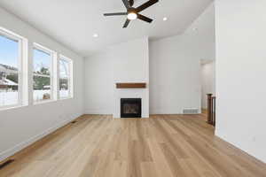 Unfurnished living room featuring light wood-style floors, vaulted ceiling, a glass covered fireplace, a ceiling fan, and recessed lighting
