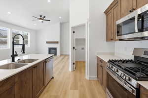 Kitchen with appliances with stainless steel finishes, a glass covered fireplace, light wood-style floors, light stone countertops, and brown cabinetry