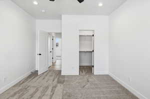 Unfurnished bedroom featuring a spacious closet, light carpet, a ceiling fan, and recessed lighting