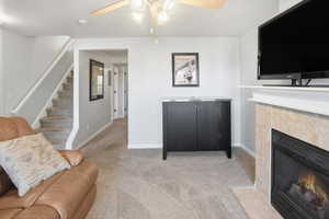 Living area featuring carpet flooring, ceiling fan, a tiled fireplace, and stairs