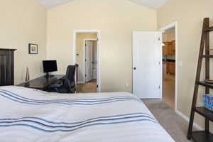 Bedroom with light carpet, vaulted ceiling, and an office area
