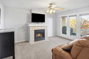 Carpeted living area with a tiled fireplace and a ceiling fan