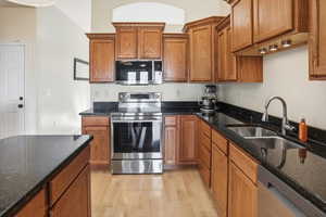 Kitchen featuring stainless steel appliances, brown cabinets, dark stone counters, and light wood-style floors