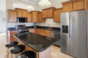 Kitchen featuring stainless steel appliances, brown cabinets, light wood-type flooring, pendant lighting, and dark stone counters