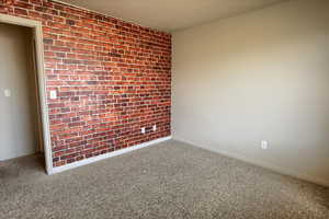 Carpeted bedroom featuring brick wall and baseboards