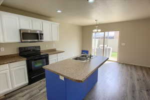 Kitchen with black range with electric stovetop, white cabinetry, stainless steel microwave, a kitchen island with sink, and recessed lighting