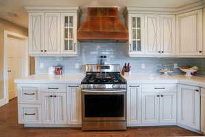 Kitchen with stainless steel gas range, premium range hood, light stone counters, and glass insert cabinets